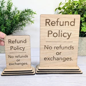 May include: Two wooden signs with the text "Refund Policy" and "No refunds or exchanges." The signs are on a wooden stand.
