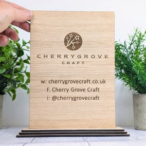 May include: A wooden sign with the text "Cherry Grove Craft" and a logo of a stylised cherry blossom tree. The sign also includes contact information: "w: cherrygrovecraft.co.uk", "f: Cherry Grove Craft", and "i: @cherrygrovecraft".