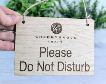 May include: A wooden sign with a brown stain and a natural wood grain. The sign has two holes at the top for hanging. The sign says "Cherry Grove Craft" and "Please Do Not Disturb".