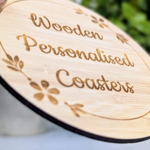 May include: A round wooden coaster with the words "Wooden Personalised Coasters" engraved in a cursive font. The coaster has a light brown color with a dark brown border and floral accents.