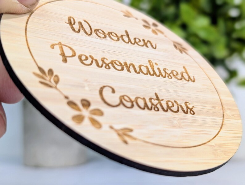 May include: A round wooden coaster with the words "Wooden Personalised Coasters" engraved in a cursive font. The coaster has a light brown color with a dark brown border and floral accents.