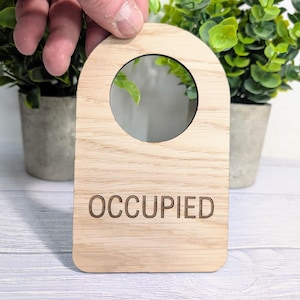 Könnte beinhalten: Ein Holztürschild mit einem runden Ausschnitt und dem Wort "BESETZT" darauf graviert.
