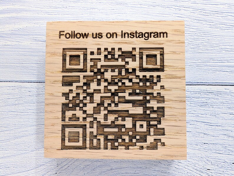 Op de afbeelding: Een houten bord met de tekst "Follow us on Instagram" en een zwart-witte QR-code.