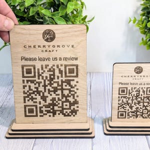 Könnte beinhalten: Zwei Holzschilder mit einem lasergravierten QR-Code und dem Text "Cherrygrove Craft. Bitte hinterlassen Sie uns eine Bewertung." Die Schilder stehen auf einer Holzoberfläche.