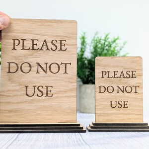 May include: Two wooden signs with the text "PLEASE DO NOT USE" on them. The signs are on a tiered stand and are made of natural wood.