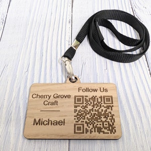 May include: Wooden name tag with a black lanyard. The tag has the text "Cherry Grove Craft" and "Michael" engraved on it. It also has a QR code with the text "Follow Us" above it.