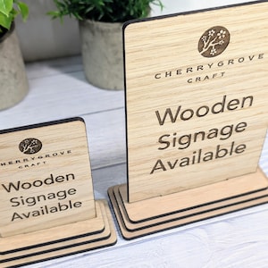 May include: Two wooden signs with a black border and a stand. The signs are made by Cherry Grove Craft and say "Wooden Signage Available".