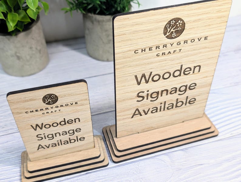 May include: Two wooden signs with a black border and a stand. The signs are made by Cherry Grove Craft and say "Wooden Signage Available".