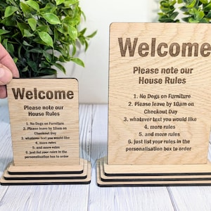 May include: Two wooden signs with the text "Welcome" and "Please note our House Rules" followed by a list of rules. The signs are on a wooden stand.