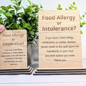 May include: Two wooden signs with the text "Food Allergy or Intolerance?" and instructions for customers with food allergies or intolerances. The signs are on a wooden base.