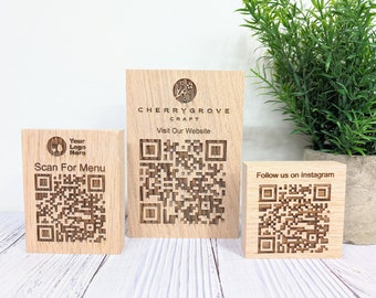 Op de afbeelding: Drie houten blokken met QR-codes en tekst. Het eerste blok zegt "Your Logo Here" en "Scan For Menu". Het tweede blok zegt "CHERRYGROVE CRAFT" en "Visit Our Website". Het derde blok zegt "Follow us on Instagram".