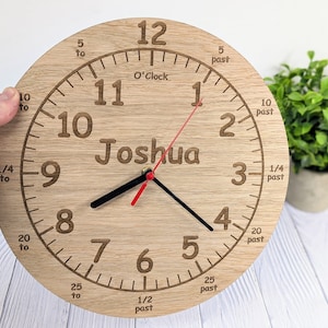 May include: A wooden clock with a light brown finish. The clock face has black Roman numerals and black hands. The clock is personalized with the name "Joshua".