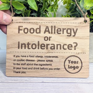 May include: A wooden sign with the text "Food Allergy or Intolerance?" and "If you have a food allergy, intolerance, or coeliac disease - please speak to the staff about the ingredients in your food and drink before you order. Thank you."  The sign also has the text "Your Logo" in a circle.