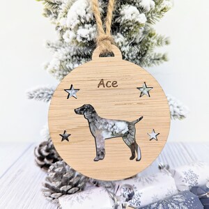 May include: A wooden Christmas ornament shaped like a circle with a cutout of a dog and the name "Ace" inscribed on it. The ornament is decorated with small stars.