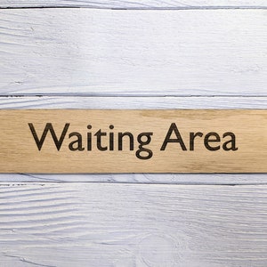 May include: A wooden sign with the text "Waiting Area" engraved on it. The sign is light brown and has a natural wood grain.