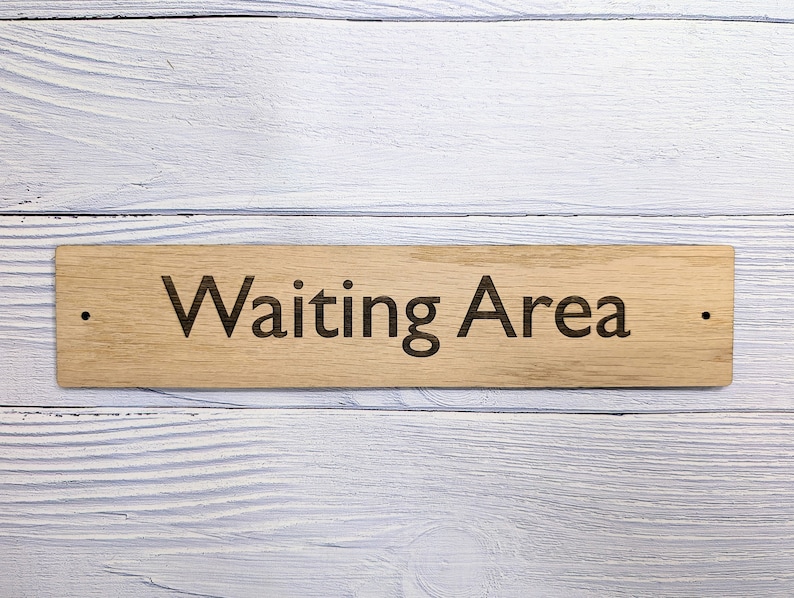 May include: A wooden sign with the text "Waiting Area" engraved on it. The sign is light brown and has a natural wood grain.