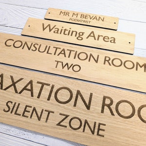 May include: Four wooden signs with engraved text. The signs are stacked in a pyramid shape. The top sign reads "Mr. M Bevan Podiatrist". The next sign down reads "Waiting Area". The third sign reads "Consultation Room Two". The bottom sign reads "Relaxation Room Silent Zone".