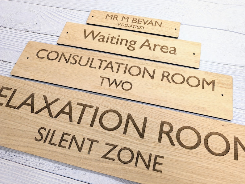 May include: Four wooden signs with engraved text. The signs are stacked in a pyramid shape. The top sign reads "Mr. M Bevan Podiatrist". The next sign down reads "Waiting Area". The third sign reads "Consultation Room Two". The bottom sign reads "Relaxation Room Silent Zone".