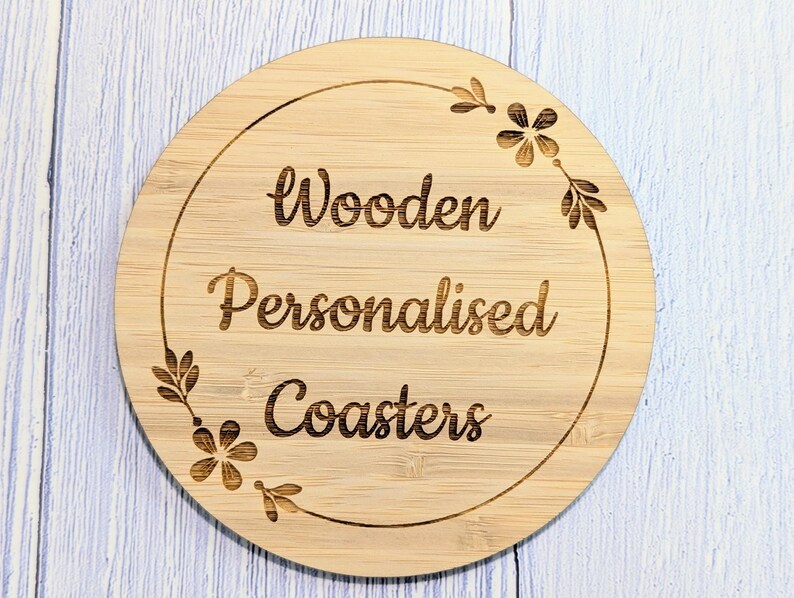 May include: A round, wooden coaster with the words "Wooden Personalised Coasters" engraved in a decorative font. The coaster has a floral design around the edge.