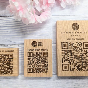 Op de afbeelding: Drie houten borden met QR-codes en tekst. Het bovenste bord zegt "CHERRYGROVE CRAFT Bezoek onze website". Het middelste bord zegt "Scan voor het menu" en het onderste bord zegt "Volg ons op Instagram".
