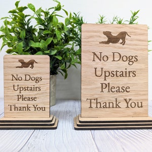 May include: Two wooden signs with the text "No Dogs Upstairs Please Thank You" and a silhouette of a dog. The signs are stacked on top of each other.