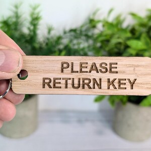 May include: A wooden key tag with the text "PLEASE RETURN KEY" engraved on it. The tag is attached to a silver key ring.