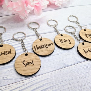May include: Six wooden keychains with different names engraved on them. The names are Ahmed, Sam, Harrison, Ruby, Pippa, and Anton. The keychains are on a light wood background.
