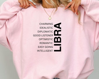May include: Pink sweatshirt with the word "LIBRA" printed vertically in black. The word is surrounded by a list of personality traits, including "charming", "idealistic", "diplomatic", "good listener", "optimistic", "romantic", "easy going", and "intelligent".