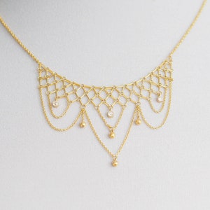 May include: A gold necklace with a delicate chain and a geometric design. The necklace features small, round beads and a dangling chain with a single bead at the end.