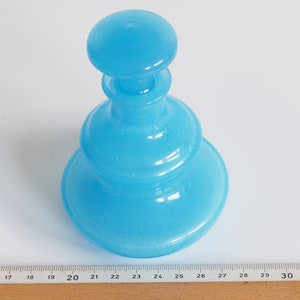 May include: A light blue glass bottle with a rounded, layered design. The bottle has a wide base and a narrow neck.
