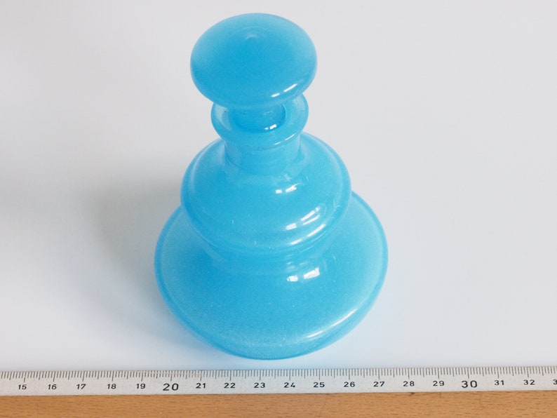 May include: A light blue glass bottle with a rounded, layered design. The bottle has a wide base and a narrow neck.