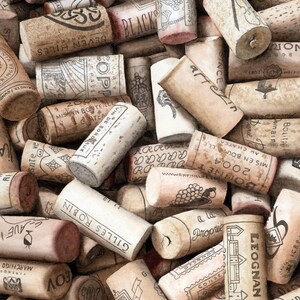 May include: A collection of numerous cylindrical wine corks stacked together. Each cork features unique branding, text, and graphic illustrations printed in black ink on the natural tan, porous surface of the cork material, showing varied wear.