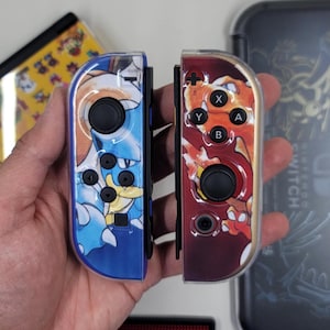 Puede incluir: Dos mandos Joy-Con de Nintendo Switch con diseños personalizados. El mando izquierdo tiene un diseño azul y amarillo con un personaje de dibujos animados. El mando derecho tiene un diseño rojo y naranja con un personaje de dibujos animados.