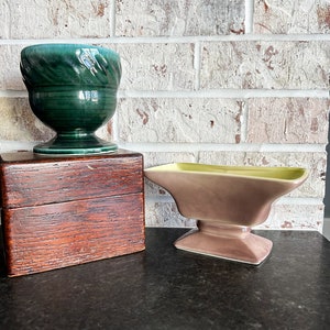 May include: Two ceramic planters, one green and one purple with a yellow rim, on a dark countertop in front of a white brick wall.