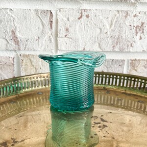 May include: A teal blue glass vase with a spiral design and a wide, flared top. The vase is sitting on a gold tray.