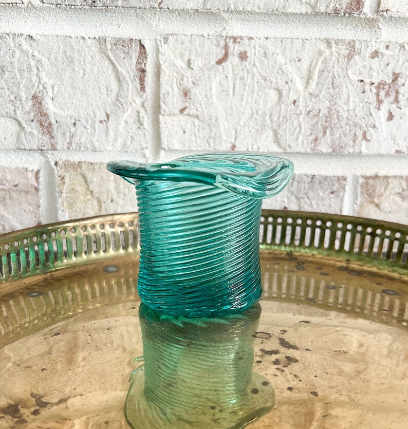 May include: A teal blue glass vase with a spiral design and a wide, flared top. The vase is sitting on a gold tray.