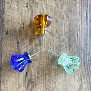 May include: Three glass cabinet knobs with metal screws. The knobs are in shades of amber, blue, and green.