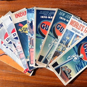May include: A collection of vintage travel maps, including Gulf Info-Maps and maps from various states. The maps feature colorful designs and text, with the Gulf logo prominently displayed on some. The maps are fanned out on a wooden surface.