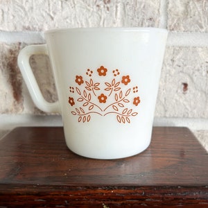 May include: White ceramic mug with a brown floral design. The design features stylized leaves and flowers.