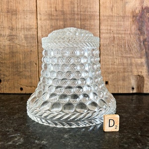 May include: Clear glass jar with a textured, bubble-like pattern. The jar has a lid with a decorative rope-like design around the top. The base of the jar has a similar design. A wooden tile with the letter "D" and the number "2" is next to the jar.