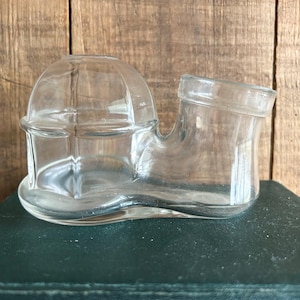 May include: A clear glass inkwell with a domed top and a separate inkwell compartment. The inkwell is shaped like a shoe.