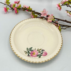 May include: A white porcelain saucer with a gold rim and a floral design featuring pink roses and green leaves.