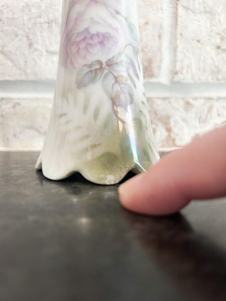 Puede incluir: Un jarr&oacute;n de porcelana blanca con base acampanada y dise&ntilde;o floral pintado. El dise&ntilde;o presenta una gran rosa de color p&uacute;rpura claro con hojas y tallos verdes. El jarr&oacute;n tiene un borde festoneado.