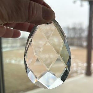 May include: A clear glass crystal prism with a faceted design. The prism is shaped like a teardrop and has a hole at the top for hanging.