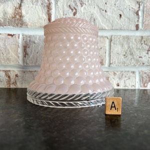 May include: A light pink glass lampshade with a textured, bubble-like pattern. The base has a decorative, clear glass trim. A wooden tile with the letter "A" and the number "1" is next to the lampshade.