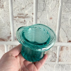 May include: A teal blue glass vase with a spiral design. The vase is shaped like a hat.