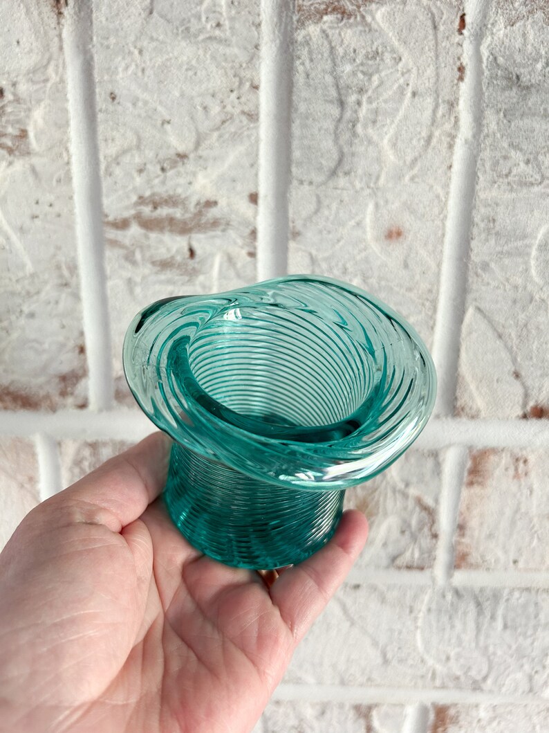 May include: A teal blue glass vase with a spiral design. The vase is shaped like a hat.