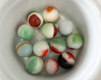 May include: A white bowl filled with colorful marbles. The marbles are a mix of green, red, white, and orange.