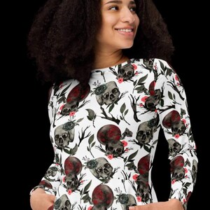 May include: White long-sleeved dress with a skull and floral print. The dress has a round neckline and two pockets.