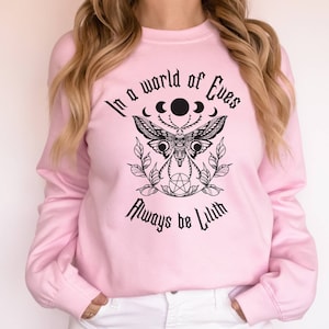 May include: Pink sweatshirt with a black graphic print of a moth, crescent moons, and a pentagram. The text reads "In a world of Eves, Always be Lilith."